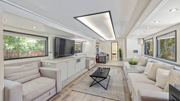 A spacious living area with a large TV, sofas, a coffee table, and a kitchen area.