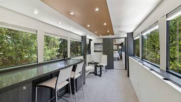 A modern interior with a bar area, seating, and large windows offering views of greenery.