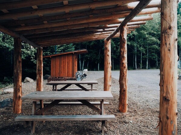 Una estructura de madera rústica con una mesa de picnic y un pequeño edificio parecido a una cabaña.