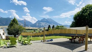 Eine Terrasse mit grünen Stühlen, einem Picknicktisch und Blick auf Berge.