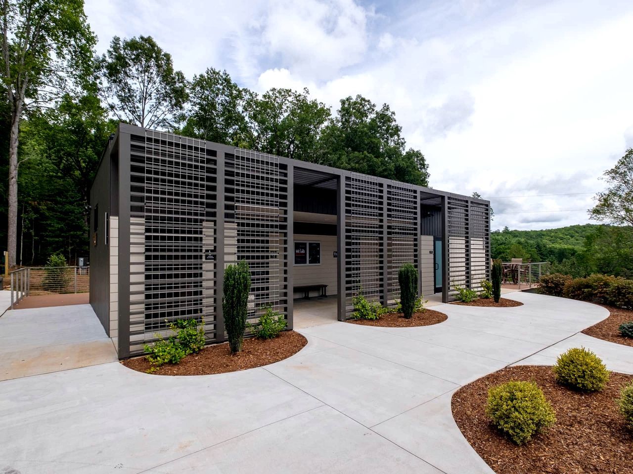 A modern building with a covered outdoor area, surrounded by landscaped gardens and trees.