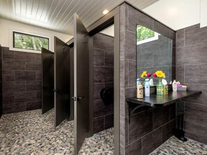 A modern bathroom with dark tiles, a vanity with toiletries, and a large mirror. - Breathtaking Invisible Tiny House in Transylvania County, North Carolina (Transylvania County)