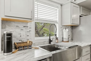 Een moderne keuken met een roestvrijstalen spoelbak, een Keurig koffiezetapparaat en een rieten mand met koffie, room en suiker.