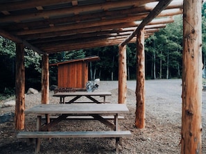 A rustic wooden structure with a picnic table and a small cabin-like building.