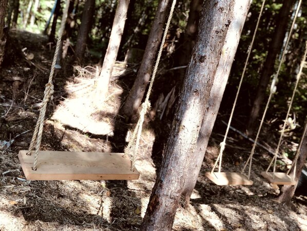 Una hamaca de madera colgada con cuerdas en un área boscosa.