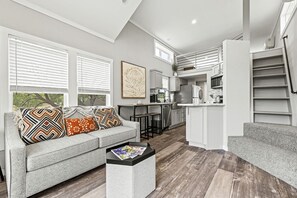 A modern living room with a grey sofa, a coffee table, and a kitchen in the background. - Picturesque Cabin with Outdoor Patio and Picnic Table in Texas (Fredericksburg)