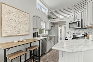 A modern kitchen with a central island, stainless steel appliances, and a large abstract painting. - Picturesque Cabin with Outdoor Patio and Picnic Table in Texas (Fredericksburg)