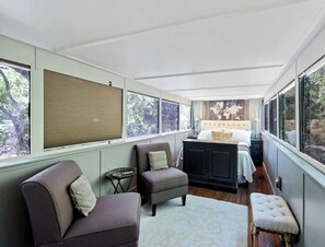 Een knus slaapkamer met een bed, twee fauteuils, een tafeltje en een raam met zonwering.