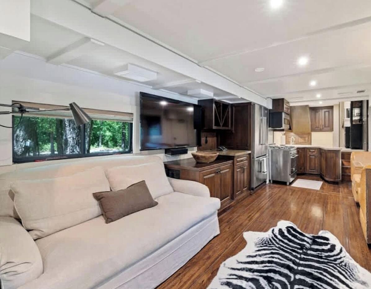 A modern RV interior with a living area, kitchenette, and a large window.