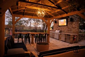 Een terras buiten met een houten pergola, zitplaatsen, een bar en een buitenkeuken.