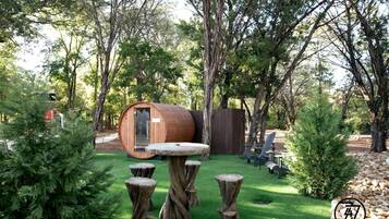 A rustic outdoor setting with a wooden barrel structure, a round table, and several wooden stools.