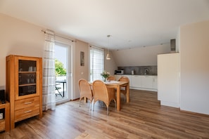 A modern kitchen with white cabinets, a dining area with a wooden table and wicker chairs, and a wooden cabinet with glass doors. - Apartment 'Kirschblüte' with Mountain View, Shared Garden and Wi-Fi (Oberkirch)