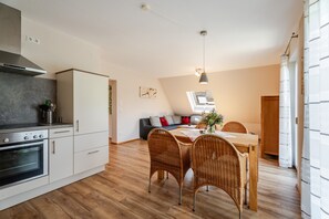 A modern kitchen with white cabinets, a built-in oven, and a dining area with wicker chairs and a wooden table. - Apartment 'Kirschblüte' with Mountain View, Shared Garden and Wi-Fi (Oberkirch)