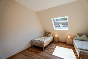 A bedroom with a sloped ceiling, a window with a view of greenery, two beds with matching pillows, and a bedside table with a lamp. - Apartment 'Kirschblüte' with Mountain View, Shared Garden and Wi-Fi (Oberkirch)