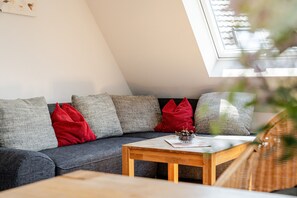 A modern loft-style living space with a sloped ceiling, a gray sectional sofa with red and gray cushions, and a wooden coffee table. - Apartment 'Kirschblüte' with Mountain View, Shared Garden and Wi-Fi (Oberkirch)