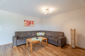 A living room with a grey sofa, a wooden coffee table, a red abstract painting, and a tall woven structure. - Apartment 'Ferienwohnung Rebblüte' with Mountain View, Shared Garden and Wi-Fi (Oberkirch)