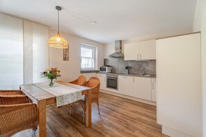 A modern kitchen with white cabinets, a dining table with wicker chairs, and a hanging light fixture. - Apartment 'Ferienwohnung Rebblüte' with Mountain View, Shared Garden and Wi-Fi (Oberkirch)