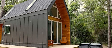 A cabin with a sloped roof, a deck, and a hot tub.