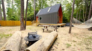 Een chalet met schuin dak, een houten terras, een picknicktafel, een hangmat en een vuurplaats.
