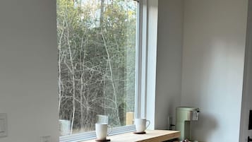 Ett kök med ett fönster, två pallar, en kaffemaskin och en hylla med koppar.