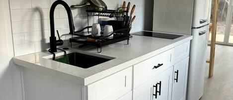 A modern kitchen with white cabinetry, a black faucet, a microwave on a wooden shelf, and a dish rack with utensils.