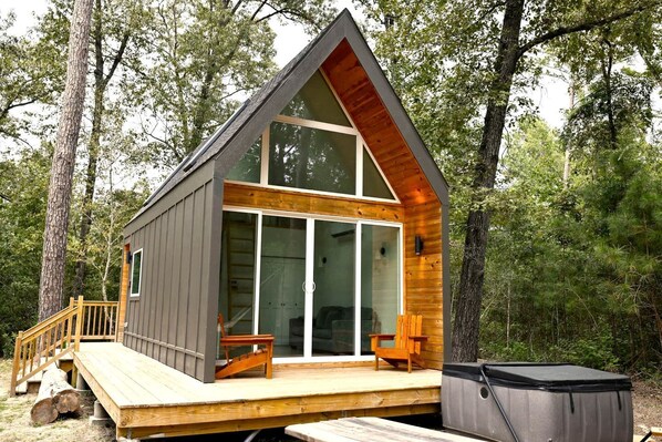 A cabin with a wooden deck, large sliding glass doors, and a hot tub.