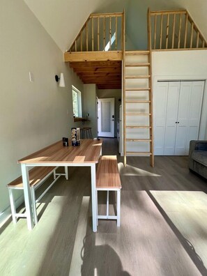 A loft-style room with a wooden staircase, a dining table, and a bench. - Impressive Cabin with Hammock in Montgomery, Texas (Montgomery)