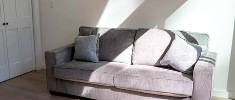 A grey sofa with patterned cushions in a room with wooden flooring and a white door.