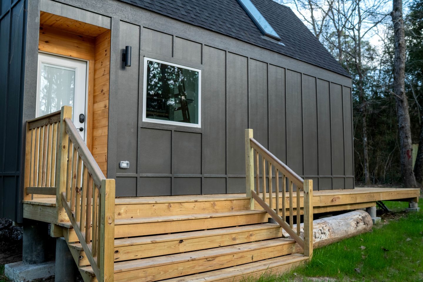 A cabin with a wooden front door, a small window, and a wooden staircase leading to a porch.