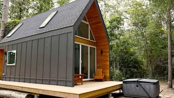 A cabin with a sloped roof, a deck, and a hot tub.