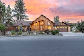 A two-story log cabin with a garage, surrounded by a landscaped garden and tall trees. - Spectacular Cabin with Foosball and Pool Table in California (Big Bear Lake)