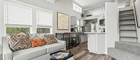 A modern living room with a grey sofa, a coffee table, and a kitchen in the background.