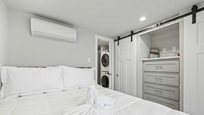 Een hotelkamer met een bed, een witte airconditioner, een wasmachine en een schuifdeurkast.