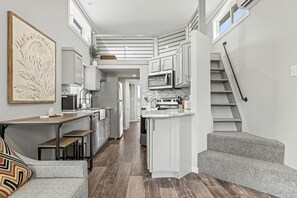 A compact kitchen with white cabinetry, a dining area with a bench, and a staircase. - Pet Friendly Cabin with Fire Pit in Fredericksburg, Texas (Fredericksburg)