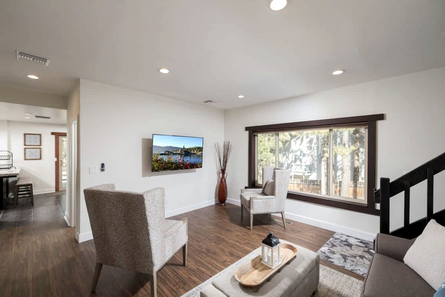 Una sala de estar moderna con un ventanal grande, un televisor de pantalla plana montado en la pared y un comedor visible al fondo.