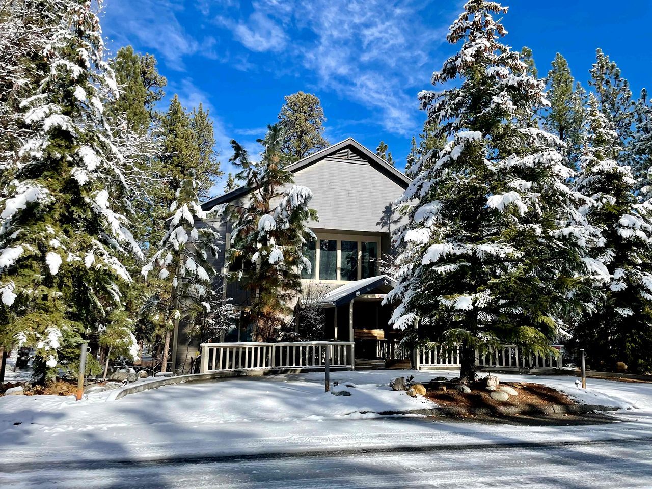A snow-covered lodge with a wooden deck and a large window overlooking a snowy landscape.