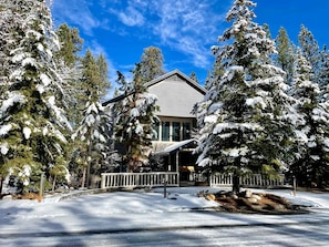 A snow-covered lodge with a wooden deck and a large window overlooking a snowy landscape. - Luxurious Cabin with Game Room, Amazing Deck and Spa in California (Big Bear Lake)