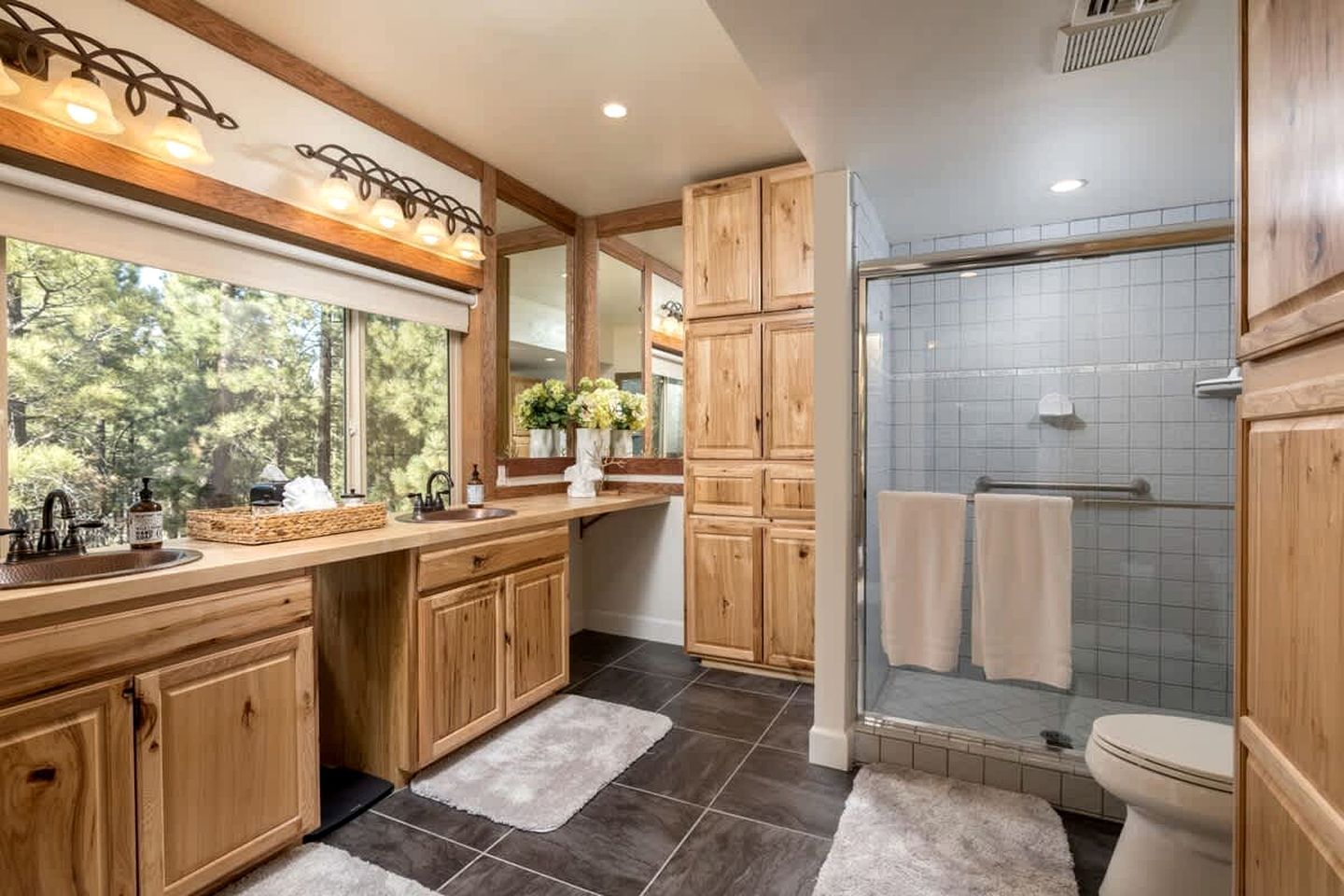 A modern bathroom with wooden cabinets, a glass shower enclosure, and a large window providing natural light.