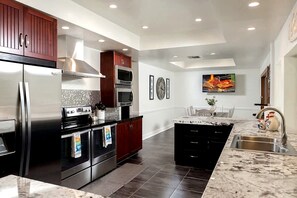 A modern kitchen with stainless steel appliances, dark wood cabinets, and a marble countertop. - Luxurious Cabin with Game Room, Amazing Deck and Spa in California (Big Bear Lake)