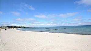 A wide sandy beach with calm waters, a clear sky, and a few buildings in the distance. - Modern vacation home with plenty of space to relax - Haus Eleganza (Glowe)