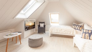 A cozy attic bedroom with a sloped ceiling, a bed, a chair, a small table, and a window. - Modern vacation home with plenty of space to relax - Haus Eleganza (Glowe)