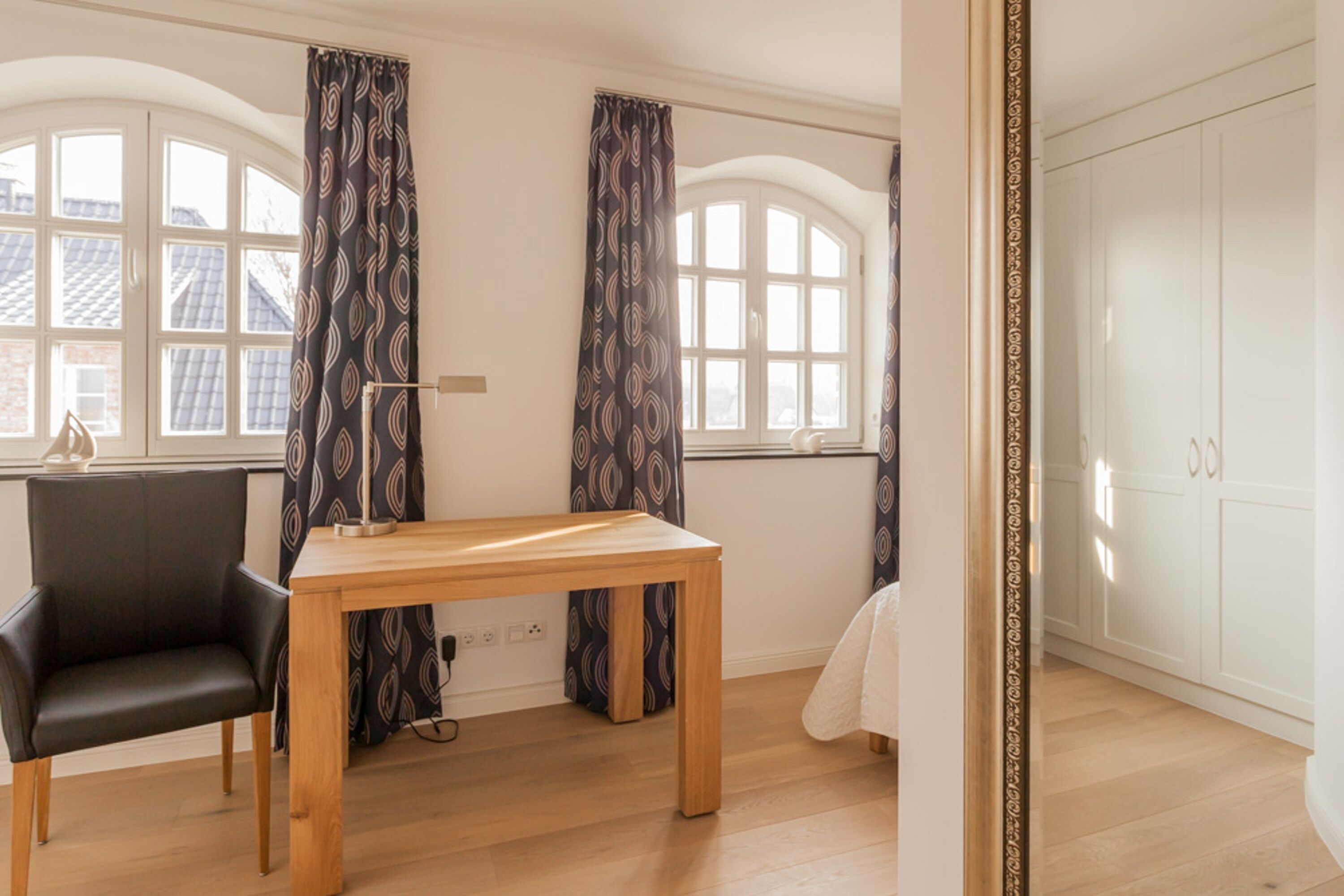 Una habitación con una mesa de madera, una silla negra y cortinas estampadas.