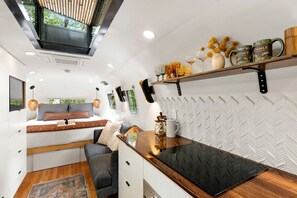A compact RV interior with a kitchenette, a bed with a view, and a dining area. - Luxury Airstream Rental for Intimate Getaways to Pisgah Forest, North Carolina (Pisgah Forest)