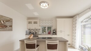 Una cocina moderna con una isla central, muebles blancos y un ventanal con cortinas.