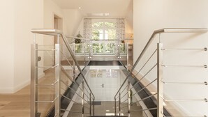 Un interior moderno con una escalera de vidrio que lleva a un balcón con vistas a zonas verdes.
