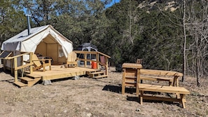 A tent with a wooden deck, a bench, and a ladder.