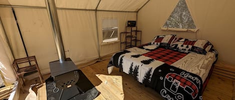 A tented room with a bed, a portable stove, a window, and a shelf with items.