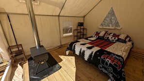 Ein Zeltraum mit Bett, einem tragbaren Kocher, einem Fenster und einem Regal mit Gegenständen.