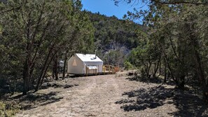 Une cabane de plain-pied, dotée d’un toit à deux versants, entourée d’une forêt dense.