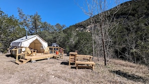 A tent with a wooden deck, a picnic table, and a chair.